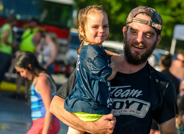 Gordon Reznicek carries his son Judah, 2, through the cool spray of water Thursday, July 2, 2026, during a free community cool off event featuring Coopersburg Fire Company's ladder truck spraying water in Coopersburg. (April Gamiz/The Morning Call)