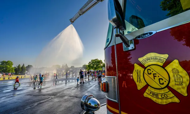 Children and families cool down under the spray Thursday, July 2, 2026, in Coopersburg during a free community cool off event featuring Coopersburg Fire Company's ladder truck spraying water. (April Gamiz/The Morning Call)