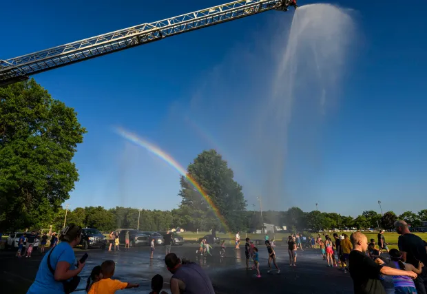 Children and families cool down under the spray Thursday, July 2, 2026, in Coopersburg during a free community cool off event featuring Coopersburg Fire Company's ladder truck spraying water. (April Gamiz/The Morning Call)