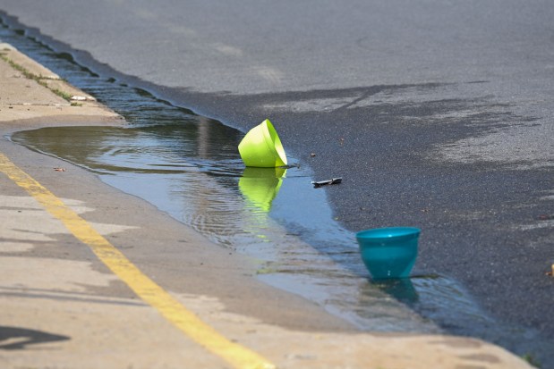 Toy buckets lie in a stream of water flowing from an open fire hydrant Wednesday, July 15, 2026, between Cottingham Stadium and Paxinosa Elementary School in Easton. Eight of the city's hydrants will be open again from noon to 6 p.m. Thursday to combat soaring temperatures. (Jon Chiu/The Morning Call)