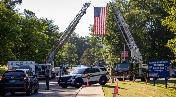 Ladder trucks display an American flag Wednesday, July 8, 2026, at the North Schuylkill Junior/Senior High School entrance as agencies gather for the funeral service for Trooper Michael Pahira Jr., who was killed in the line of duty. (AISHWARYA BEHL/STAFF PHOTO)