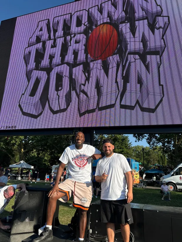 A-Town Throwdown co-directors Toomey Anderson and Randy Atiyeh pose by a giant video board alongside Court 1 at Cedar Beach as the boys basketball tournament attracted a large crowd on Thursday night. The tourney continues through Sunday. (Keith Groller)