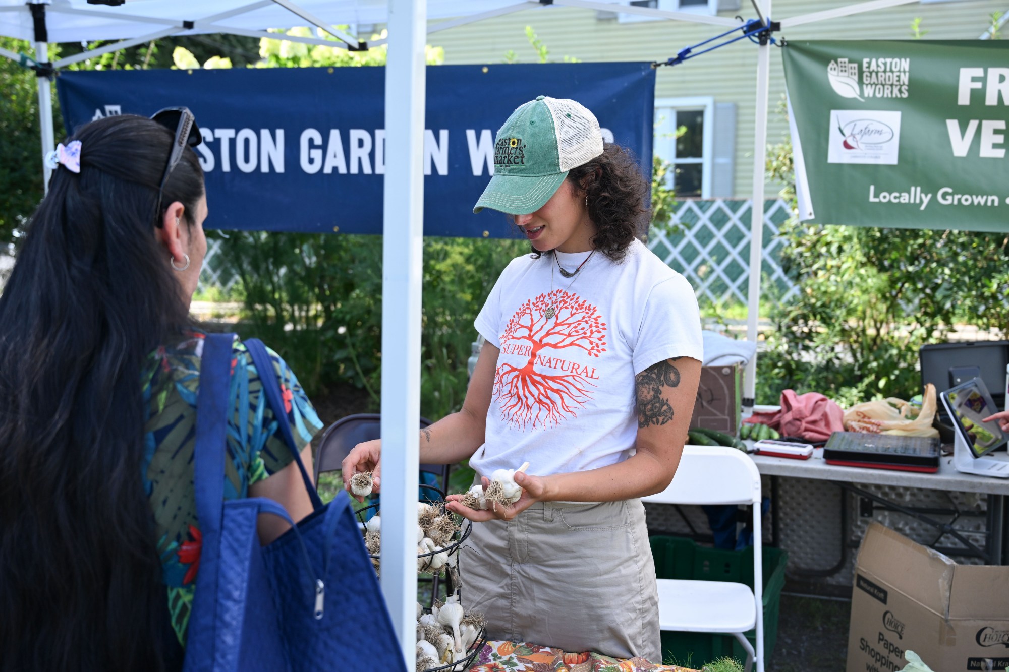 Inbal Sella, the assistant farm manager of Easton Garden Works, holds up bulbs of garlic during the 20th Annual Zucchini on 500 Thursday, July 23, 2026 at the 10th & Pine street community garden in Easton. According to West Ward Community Initiative manager Jacob Behler, events like the 'Zuke 500' are meant to help foster new community connections and help people have affordable and local access to healthy produce. (Jon Chiu/The Morning Call)