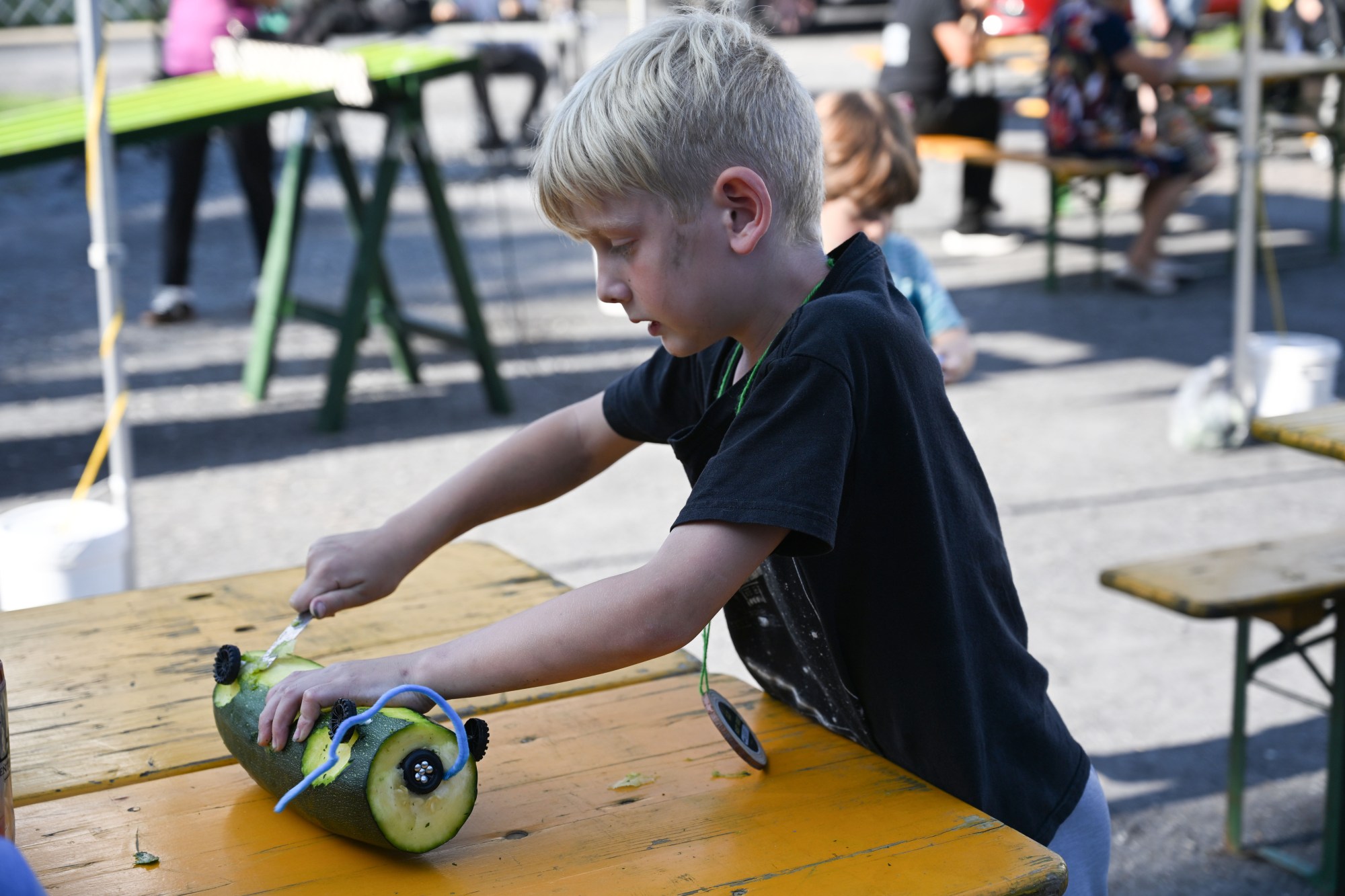 Henry Nees, 8, works on his zucchini car during the 20th Annual Zucchini 500 on Thursday, July 23, 2026 at the 10th & Pine street community garden in Easton. According to West Ward Community Initiative manager Jacob Behler, events like the 'Zuke 500' are meant to help foster new community connections and help people have affordable and local access to healthy produce. (Jon Chiu/The Morning Call)