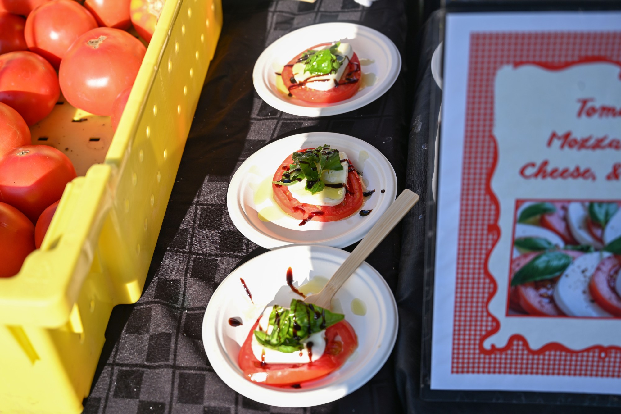 Dishes of tomatoes, basil and mozzarella cheese are lined up next to a crate of uncut tomatoes during the 20th Annual Zucchini 500 on Thursday, July 23, 2026 at the 10th & Pine street community garden in Easton. According to West Ward Community Initiative manager Jacob Behler, events like the 'Zuke 500' are meant to help foster new community connections and help people have affordable and local access to healthy produce. (Jon Chiu/The Morning Call)