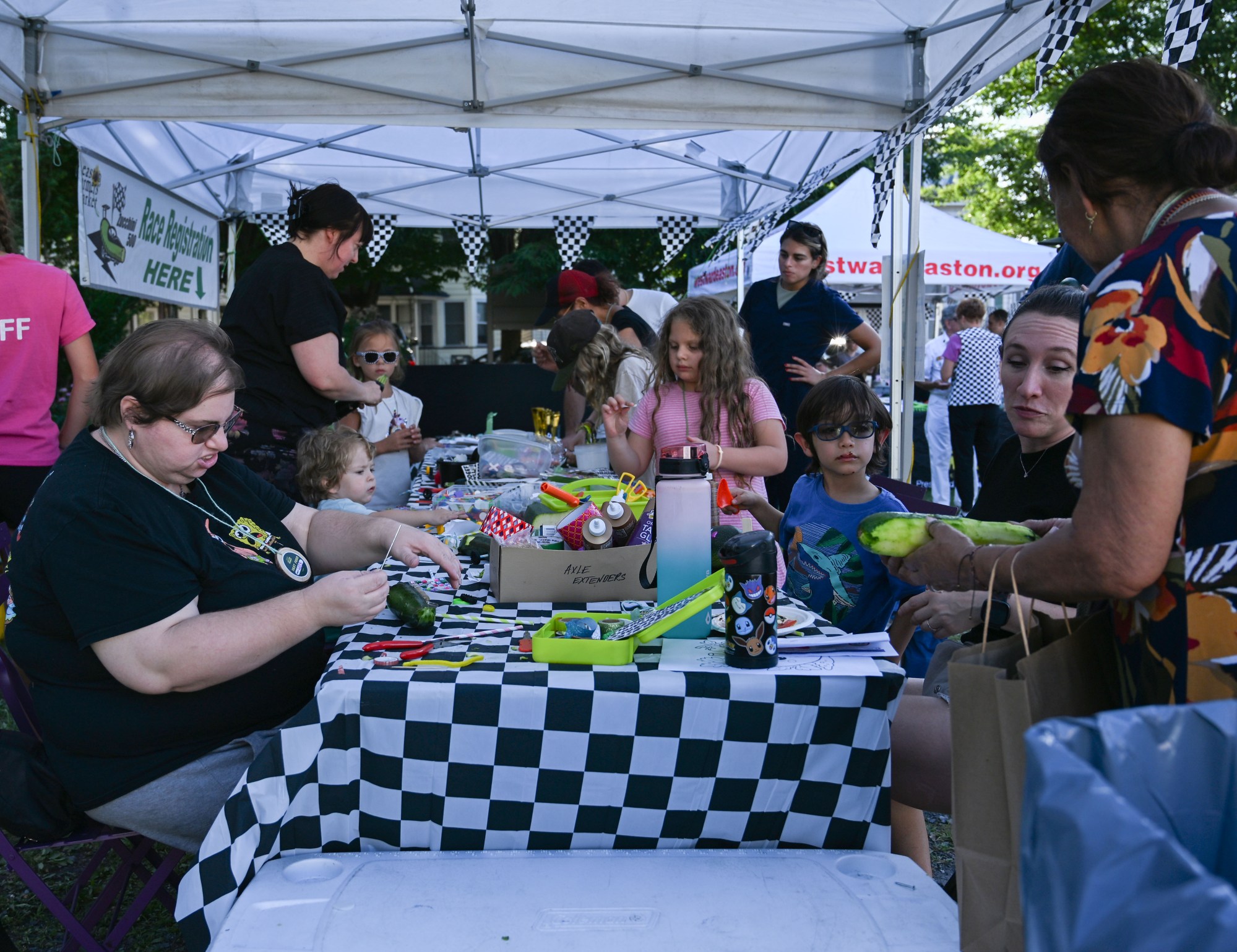Children and adults work on zucchini cars during the 20th Annual Zucchini 500 on Thursday, July 23, 2026 at the 10th & Pine street community garden in Easton. According to West Ward Community Initiative manager Jacob Behler, events like the 'Zuke 500'  are meant to help foster new community connections and help people have affordable and local access to healthy produce. (Jon Chiu/The Morning Call)