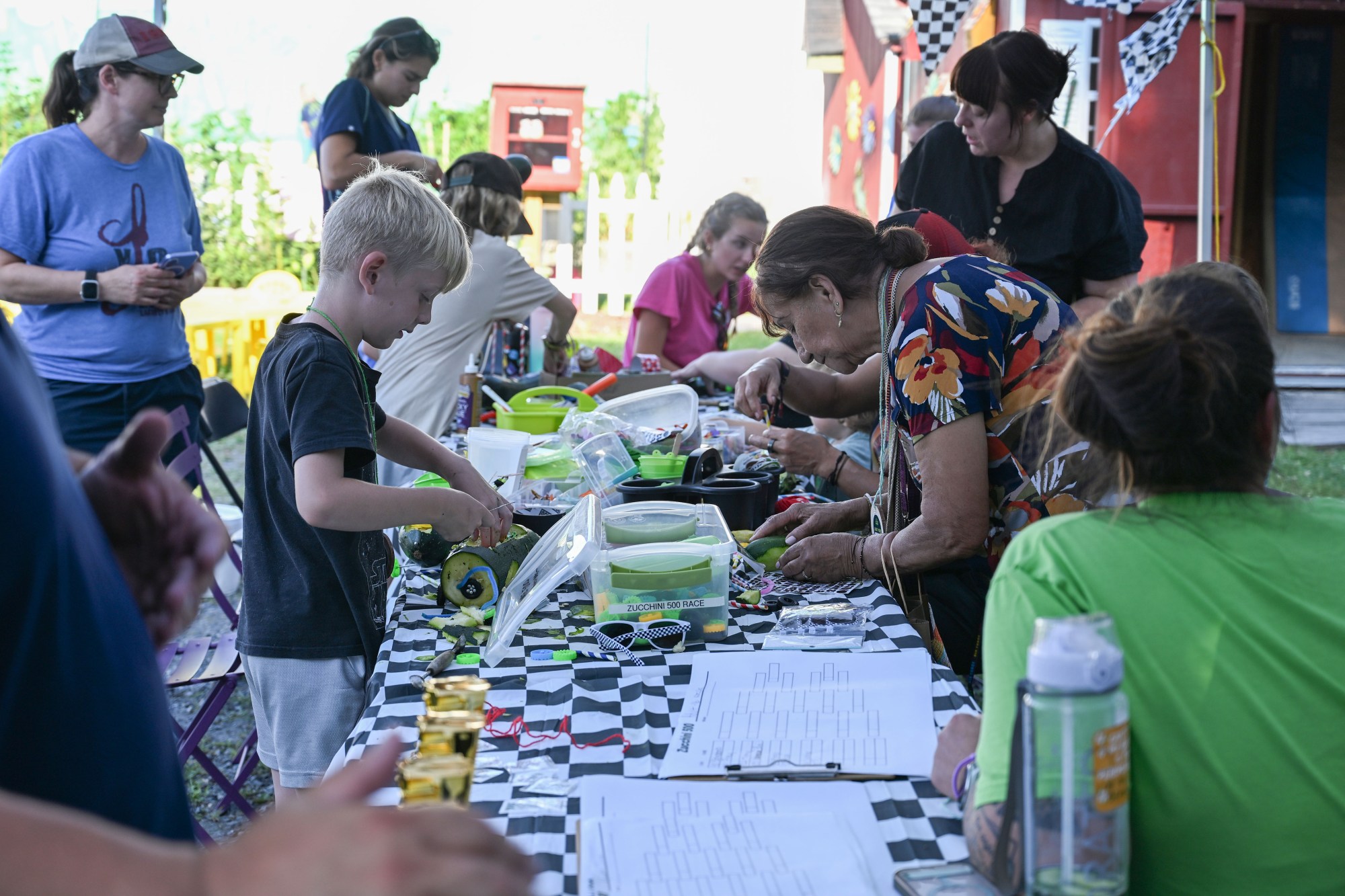 Children and adults work on zucchini cars during the 20th Annual Zucchini 500 on Thursday, July 23, 2026 at the 10th & Pine street community garden in Easton. According to West Ward Community Initiative manager Jacob Behler, events like the 'Zuke 500'  are meant to help foster new community connections and help people have affordable and local access to healthy produce. (Jon Chiu/The Morning Call)