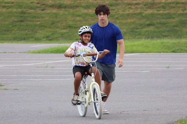 iCanBike volunteer Henry Knorp supervises Jax O'Leary of Easton, 8, as a rides a bicycle Wednesday, July 29, 2026, in the back parking lot of Easton Area High School in Palmer Township. iCanBike will remain at the high school to teach individuals with various disabilities how to ride both training and conventional bicycles until Friday. (Jon Chiu/The Morning Call)