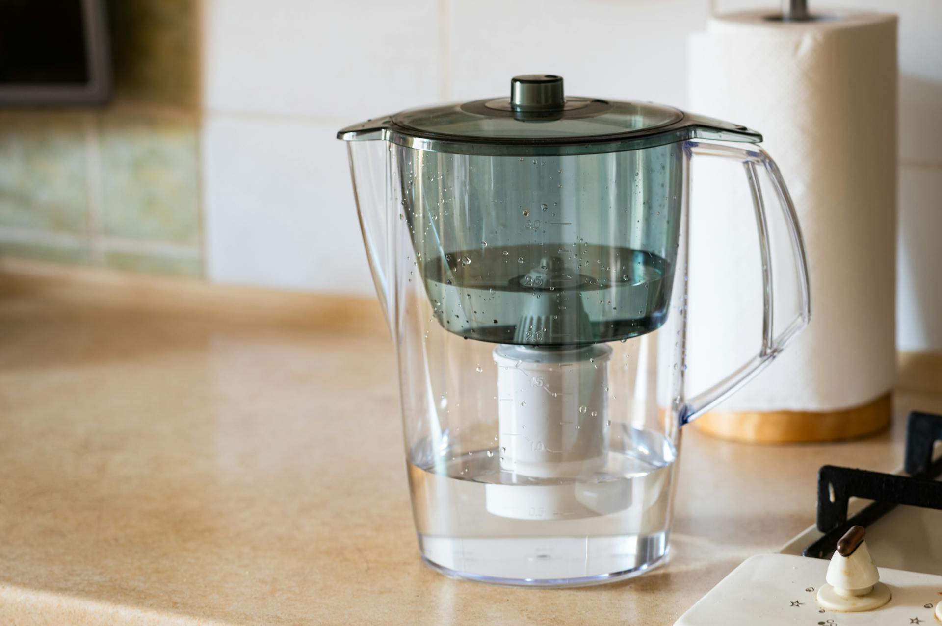 A clear plastic water filter sits on a counter beside a roll of paper towels