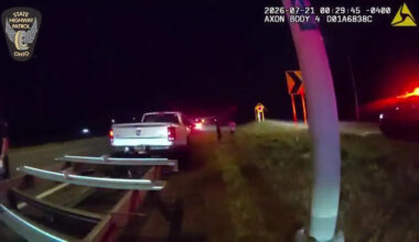 Seen here in body camera video is a white Dodge Ram 3500 pickup truck with a flatbed trailer stopped on the shoulder of the highway