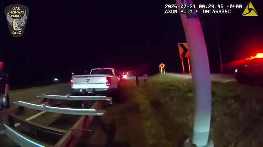 Seen here in body camera video is a white Dodge Ram 3500 pickup truck with a flatbed trailer stopped on the shoulder of the highway