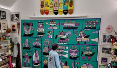 An artist stands barefoot in a studio looking at a large green mural depicting cartoon characters.