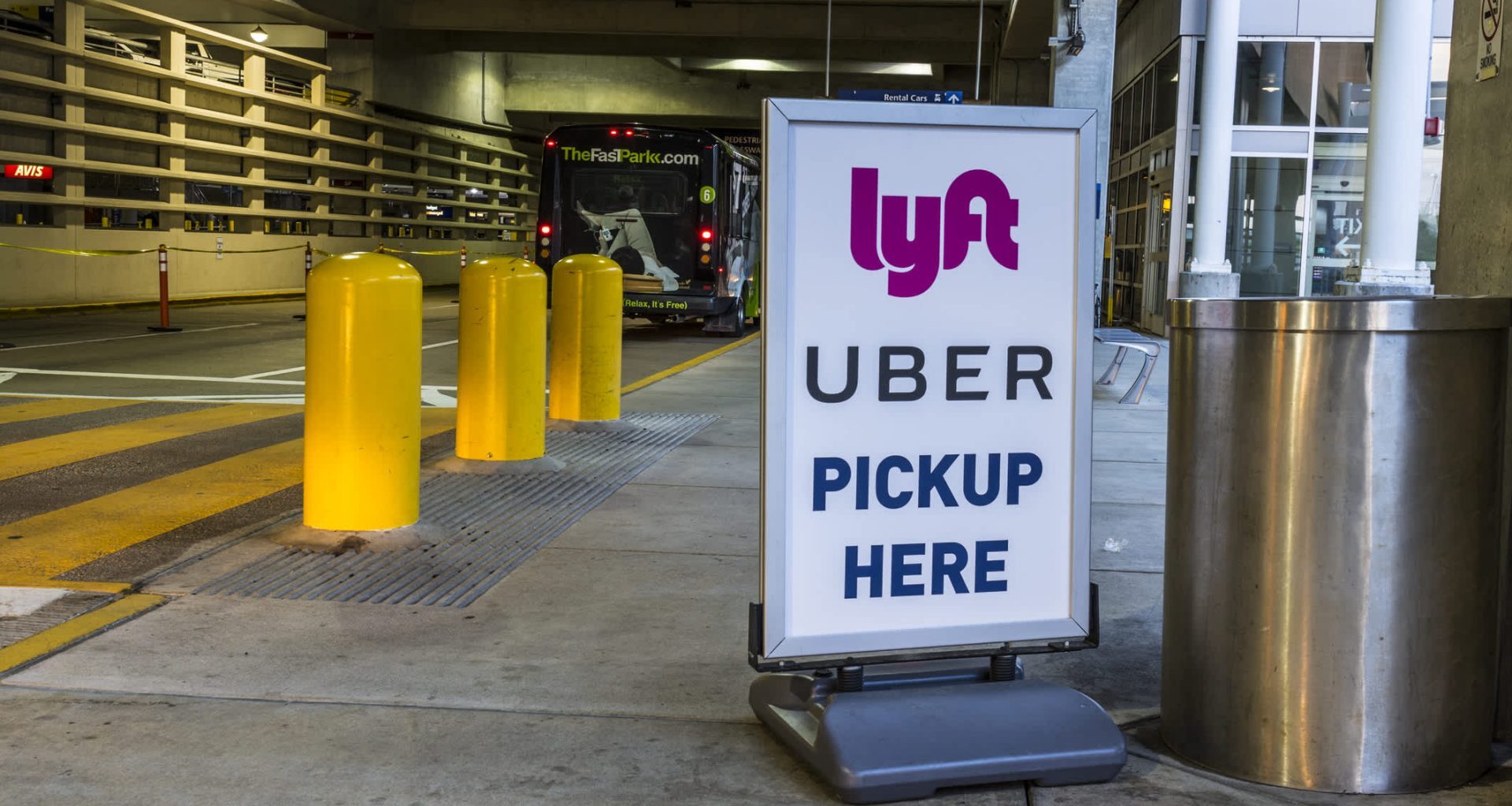 A sign indicating Uber and Lyft pickup locations at a parking area, with yellow bollards nearby.