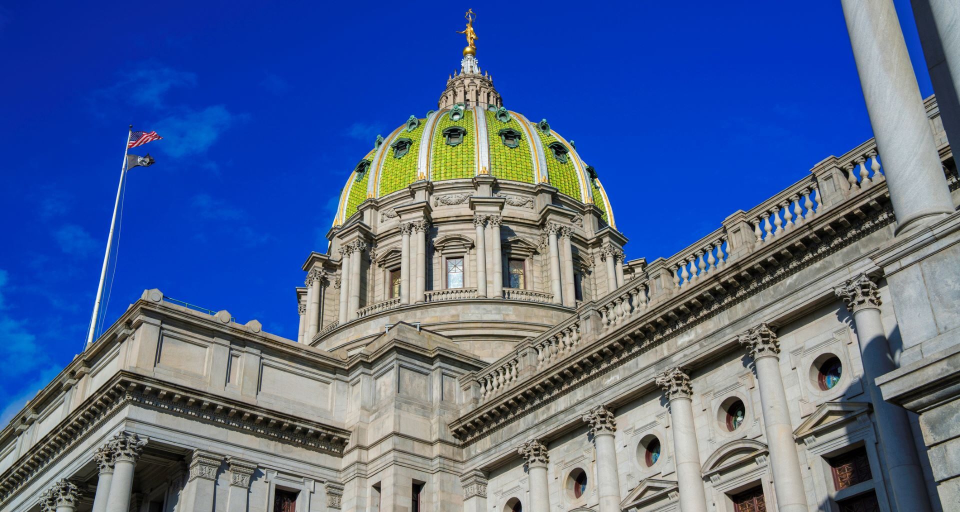 A close-up view of a grand building’s dome with a green and gold design against a clear blue sky.