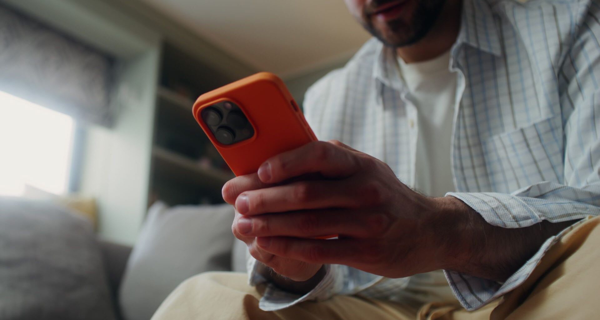 A man sitting on a couch, using an orange smartphone.