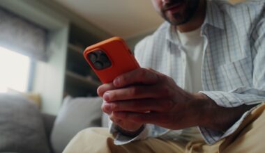 A man sitting on a couch, using an orange smartphone.