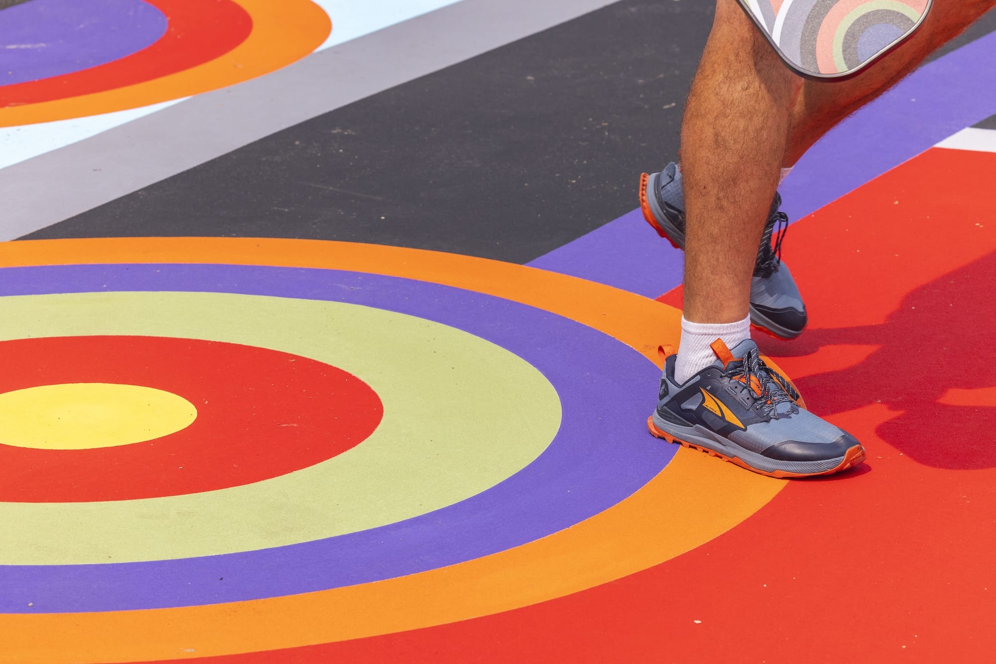 a detail of a pickleball court that has been painted with a bright geometric mural, with a person walking across it