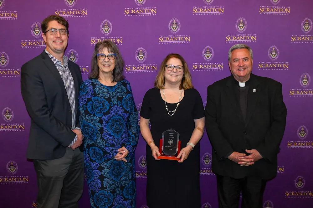 Four people pose at a University of Scranton event in front of a purple step-and-repeat backdrop.