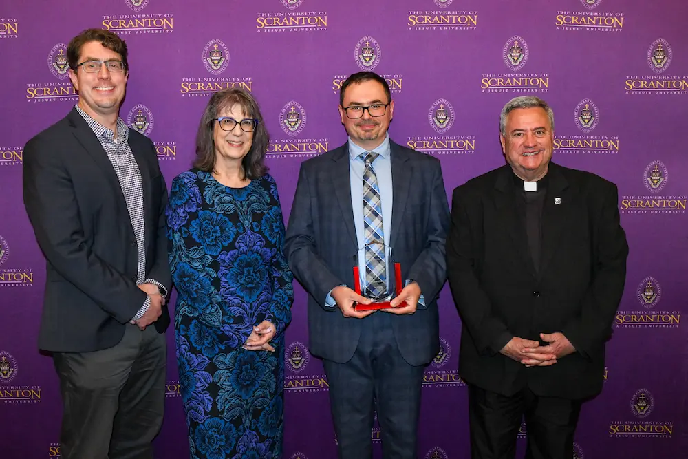 Four people pose at a University of Scranton event in front of a purple step-and-repeat backdrop.