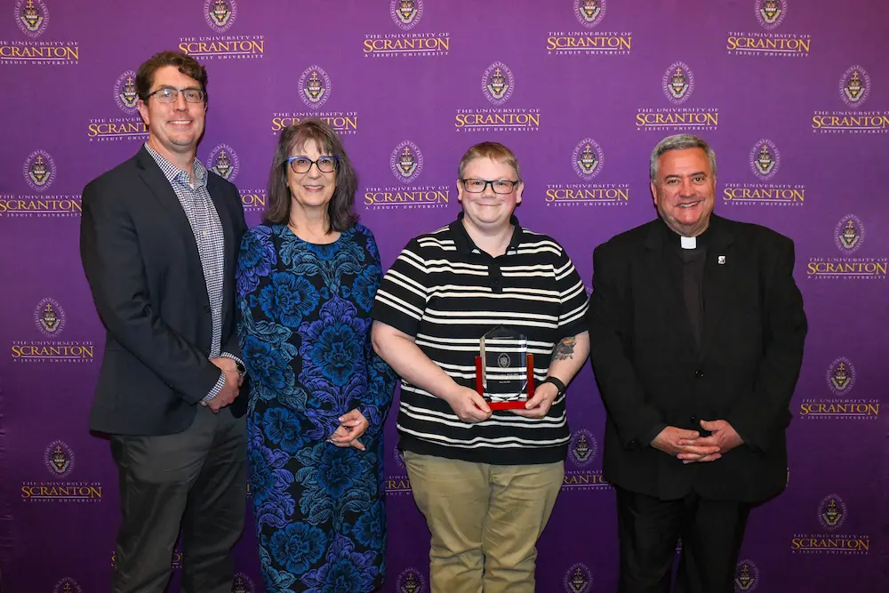 Four people pose in front of a University of Scranton step-and-repeat backdrop.