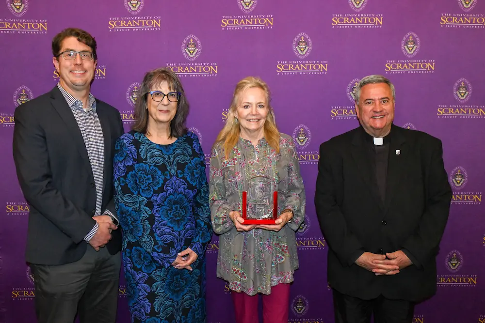 Four people pose at a University of Scranton event in front of a purple step-and-repeat backdrop.
