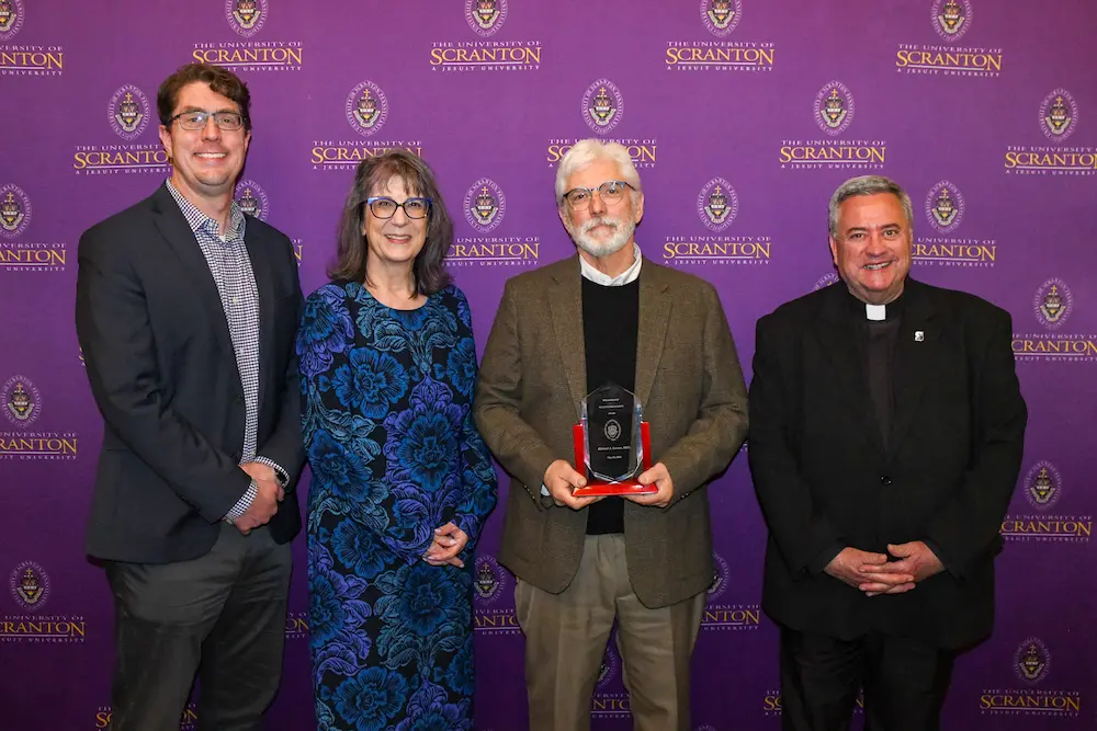Four people pose in front of a purple University of Scranton step-and-repeat backdrop.