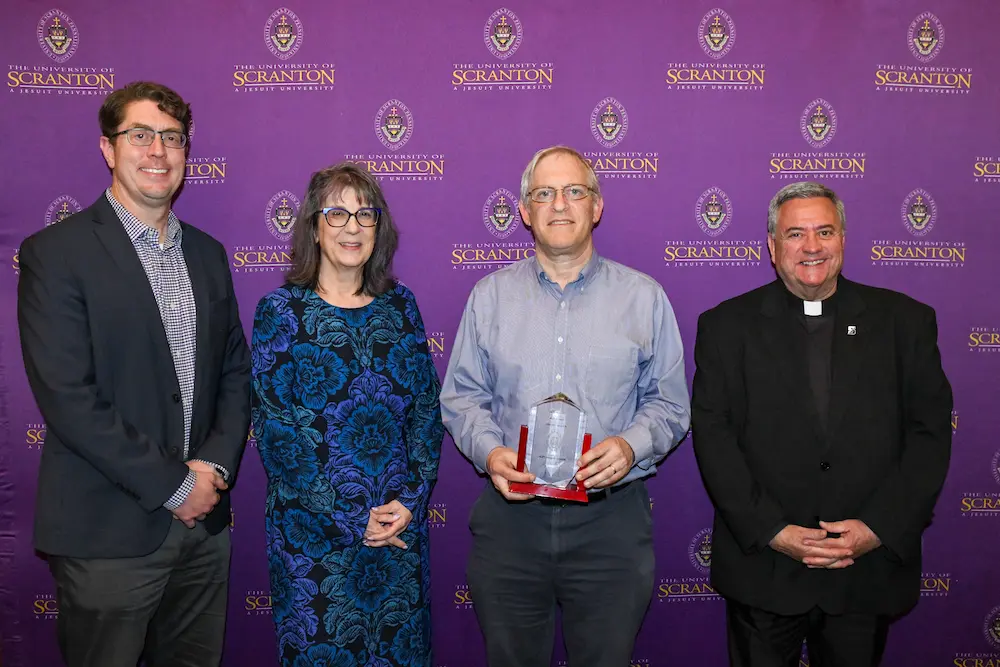 Group of four people pose in front of a University of Scranton step-and-repeat backdrop