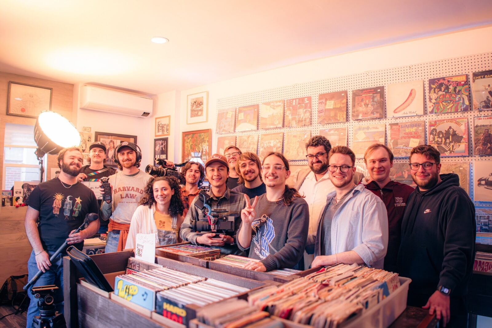 A group of people posing with camera equipment behind record bins inside a vinyl record shop.