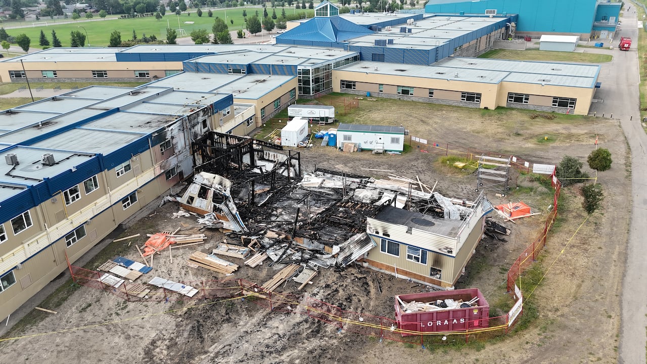 Drone images show a white and blue building next to a burned structure and construction materials.