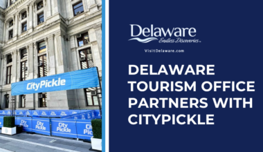 Half the screen features an image of City Hall in Philly, the other half has the DE Tourism Office logo on a dark blue background.