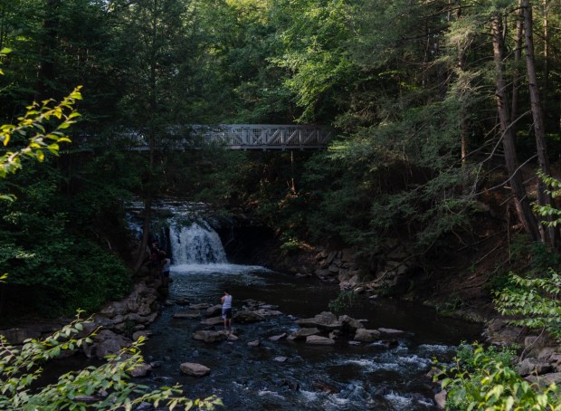 A person walks on the rocks near the waterfall at Sweet Arrow Lake County Park, Monday, June 23, 2025. (FILE)