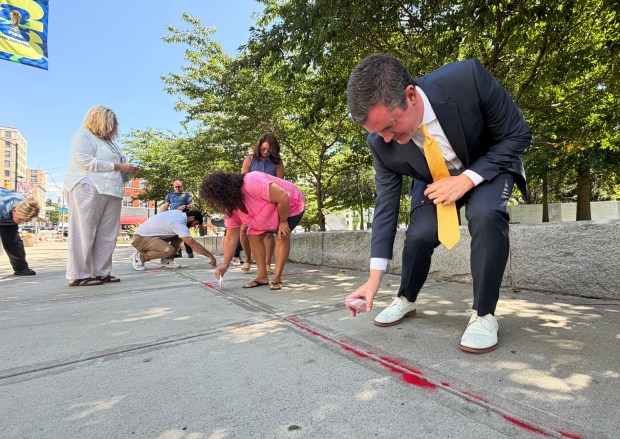 Lackawanna County Deputy District Attorney Bo Loughney pours red sand through the cracks of the sidewalk of North Washington Avenue during the Red Sand Project human trafficking and exploitation awareness event on Courthouse Square in Scranton Wednesday, August 26, 2026. (SEAN MCKEAG / STAFF PHOTOGRAPHER)