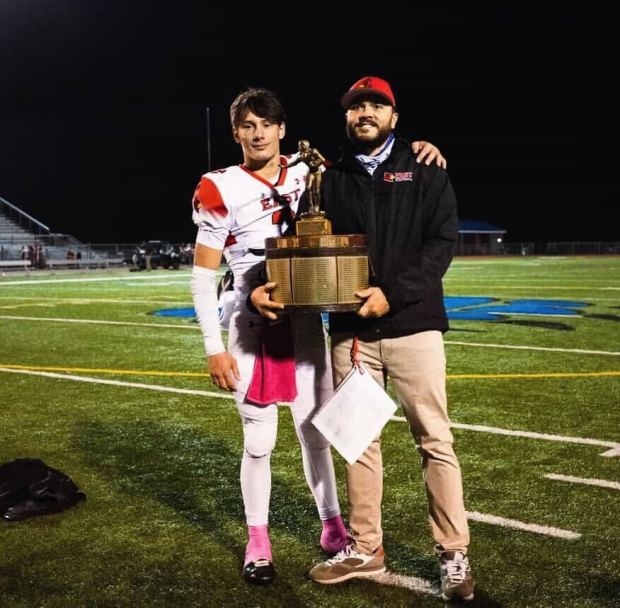 Pocono Mountain East quarterback Ceejay Serfass (left) and Cardinals coach Dustin Thomas pose with the Old Oaken Bucket trophy after East defeated Pleasant Valley 28-0 on Oct. 10. (Contributed photo / Pocono Mountain East)