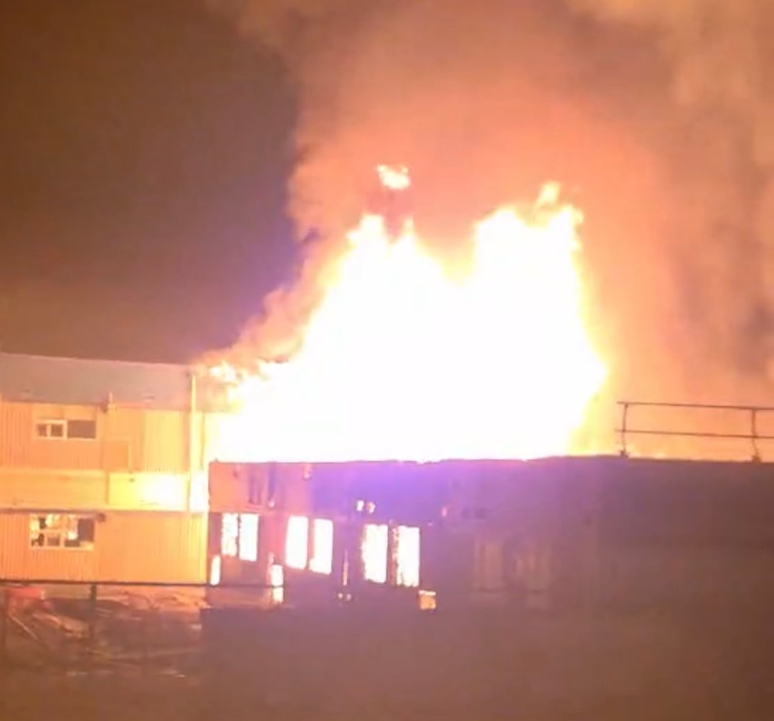 A bright blaze is ignited on the top of the school's portable classrooms. The building looks charred and damaged.