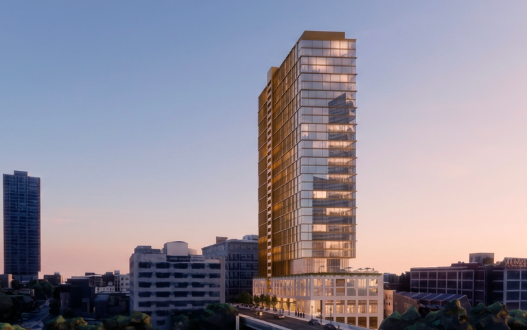 Tall modern skyscraper with glass facade in an urban setting, captured during sunset, with buildings and a road in the foreground.