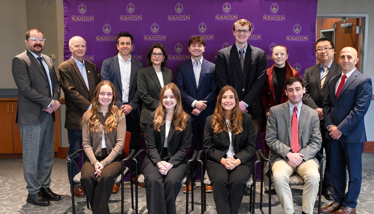 Group of students and faculty posed for a formal photo in front of a purple University of Scranton backdrop.