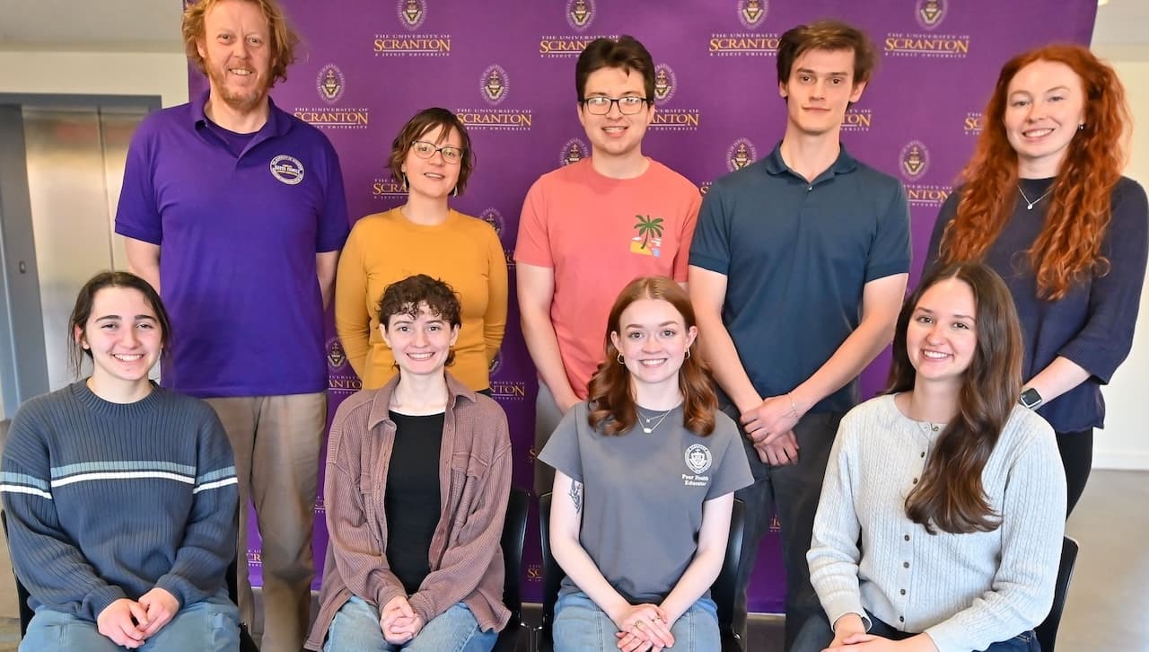 Group of people posing in front of a purple University of Scranton step-and-repeat backdrop.