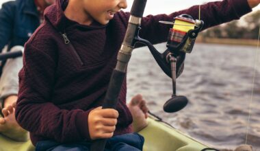 A child holding a fishing rod on a kayak with water in the background.