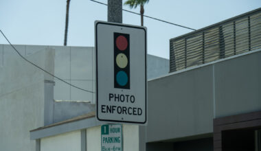 A traffic sign indicating "Photo Enforced" with red, yellow, and blue lights.