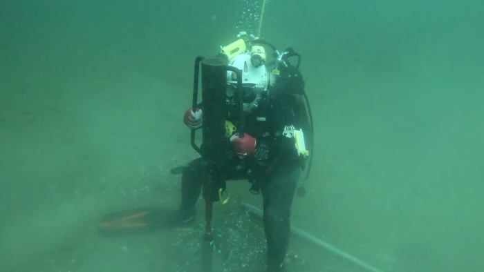 A person in scuba gear underwater holds a piece of equipment.