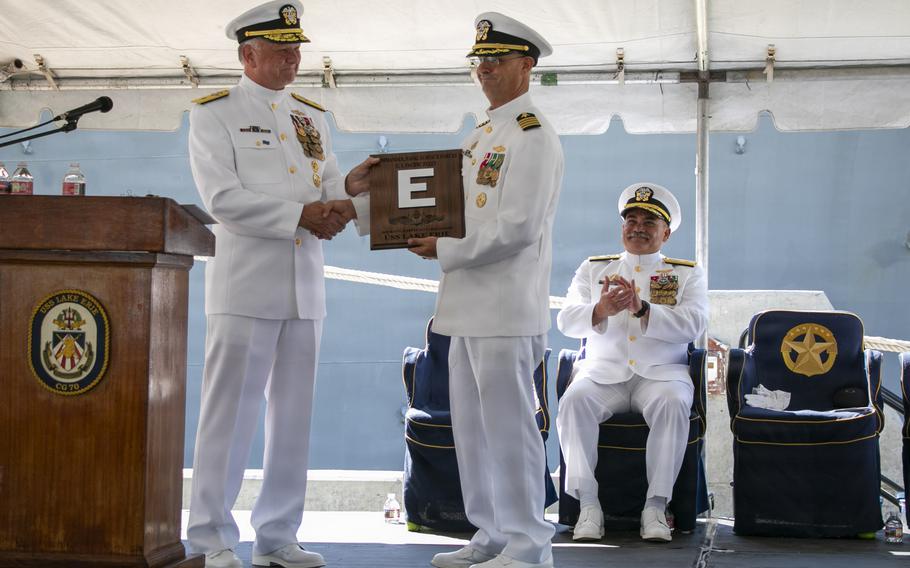 A sailor hands another sailor a plaque with a silver “E” on it.