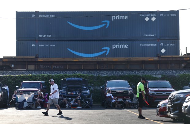 With Prime shipping containers seen atop a freight train, a Chicago White Sox fan walks through the C Lot before attending a game between the Sox and the Pittsburgh Pirates at Rate Field in Chicago on Sept. 8, 2026. Amtrak's plan calls for a new, four-story maintenance facility along a railroad viaduct just north of 35th Street. The property is currently used by the Union Pacific railroad. (Chris Sweda/Chicago Tribune)