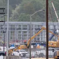 A construction site on a metal frame building. In the front are cranes and white pick-up trucks.