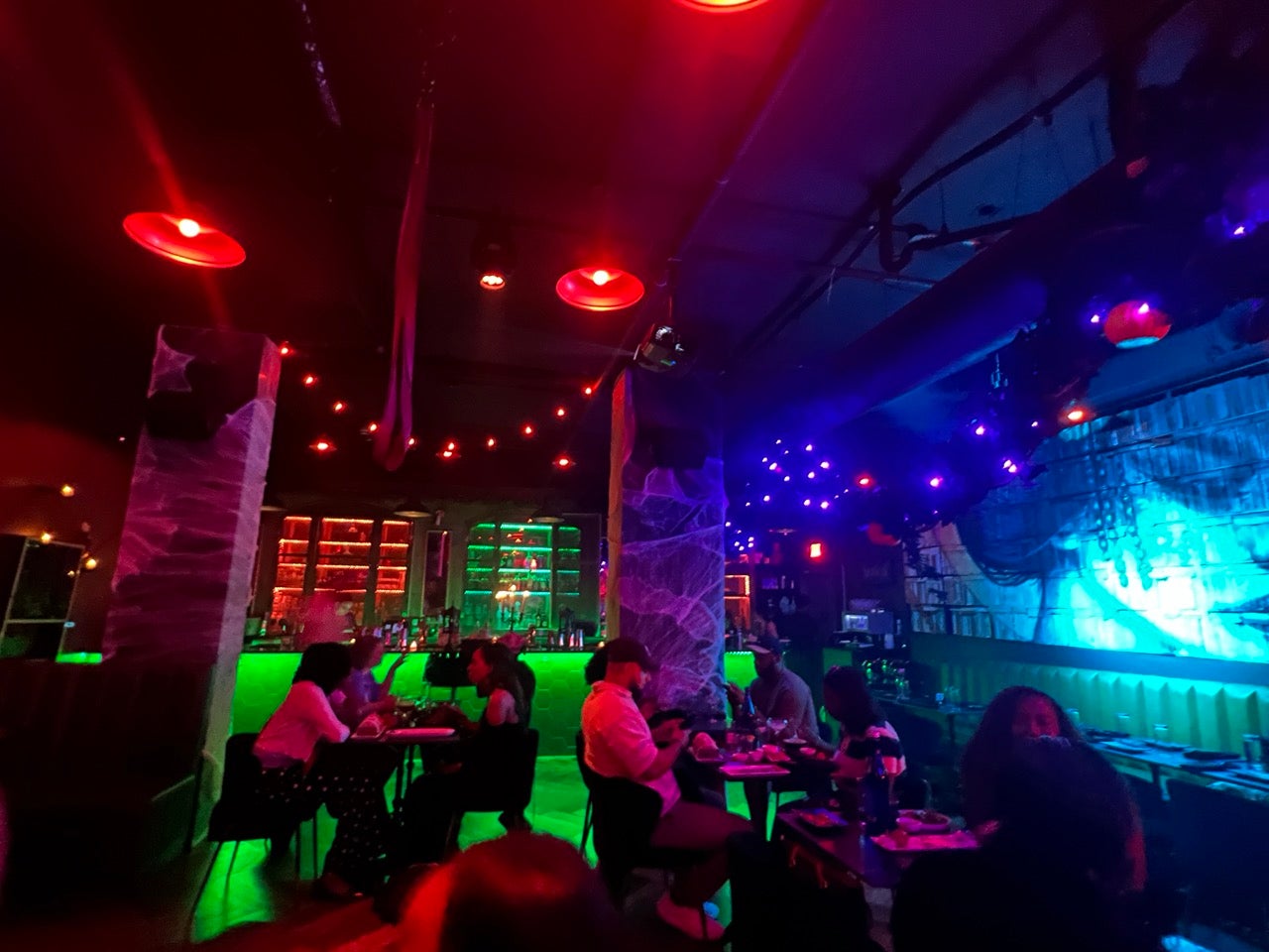 The inside of Newsroom Philadelphia's spooky Pumpkin Press Immersive restaurant and cocktail bar. Dimly lit with lots of red and green and purple.The bar in the back of the room.