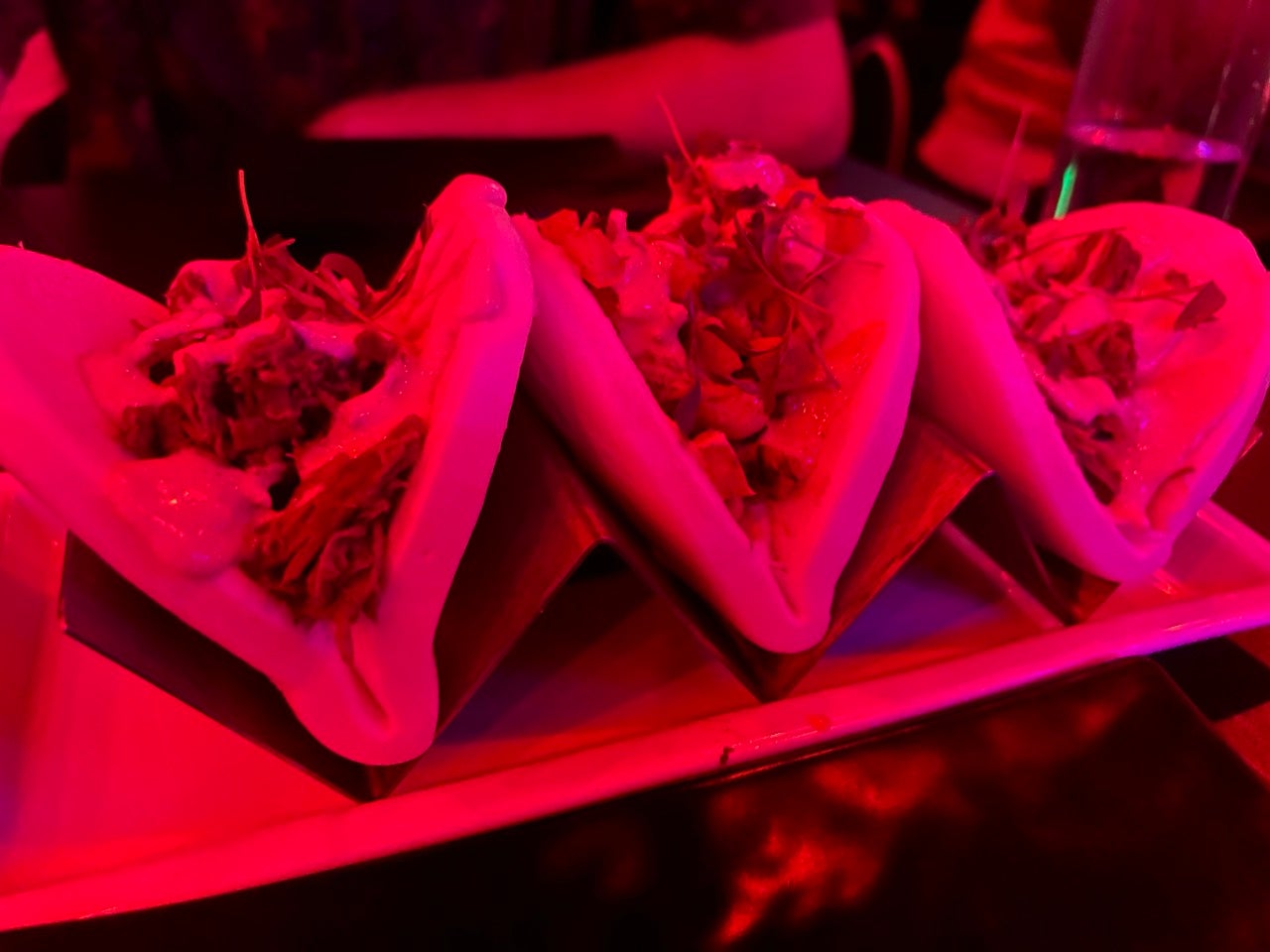 A tray of 3 delicious looking bao buns in a glowing red dimly lit dining space at Newsroom Philadelphia.