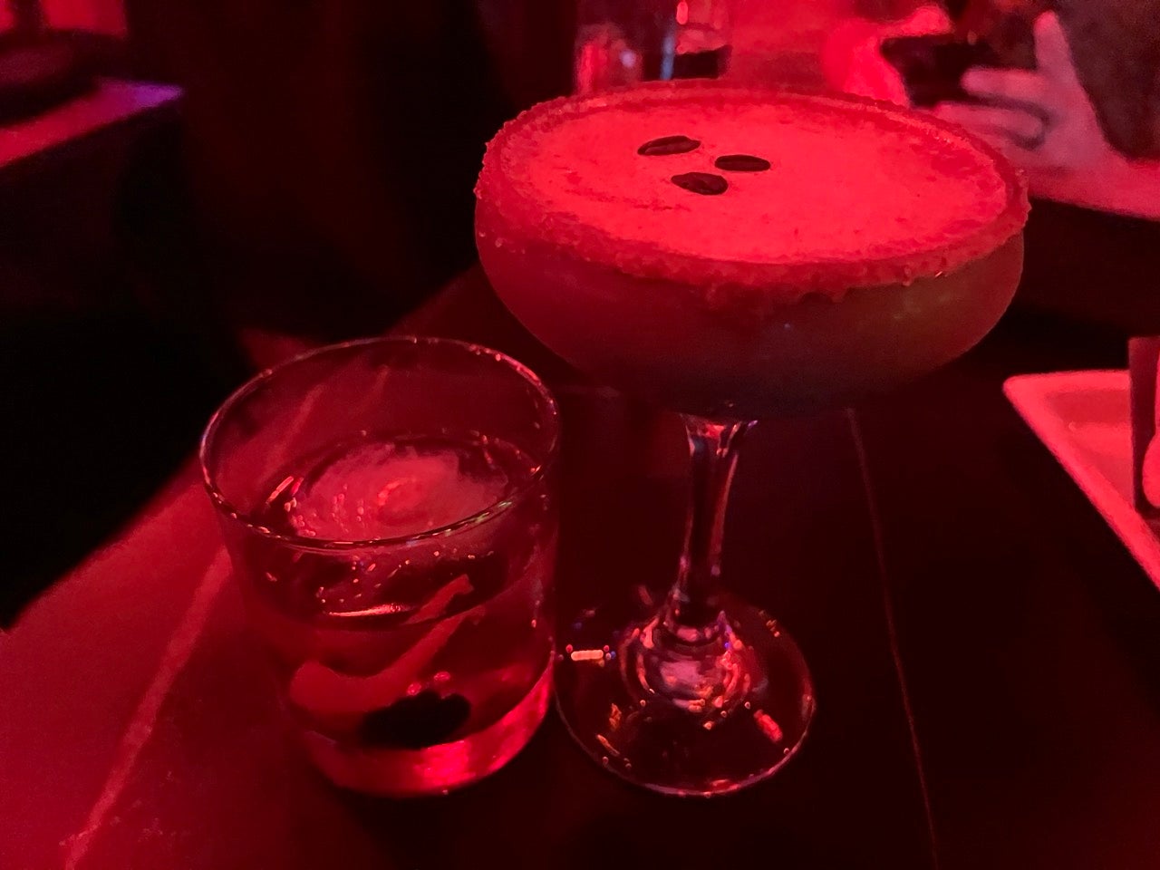 Glowing red lighting with a beautiful looking pumpkin espresso martini next to a pumpkin spice old fashioned in a glass.