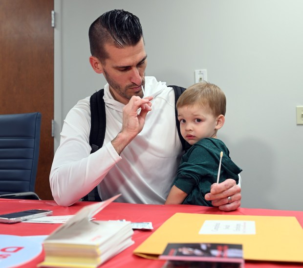 Josh Forry swabs while holding his son, Jayden, 2, during a stem cell donor registration drive at RE/MAX, 1290 Broadcasting Road, Wyomissing, on Saturday, Sept. 26, 2026. (BILL UHRICH/READING EAGLE)