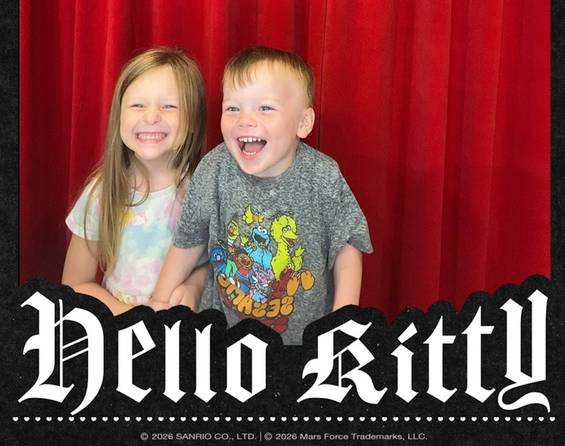 Kristen's kids smile in the photo booth set up in the Bruno Mars and Hello Kitty pop-up merch shop. Hello Kitty is in text below their photo with a read background.