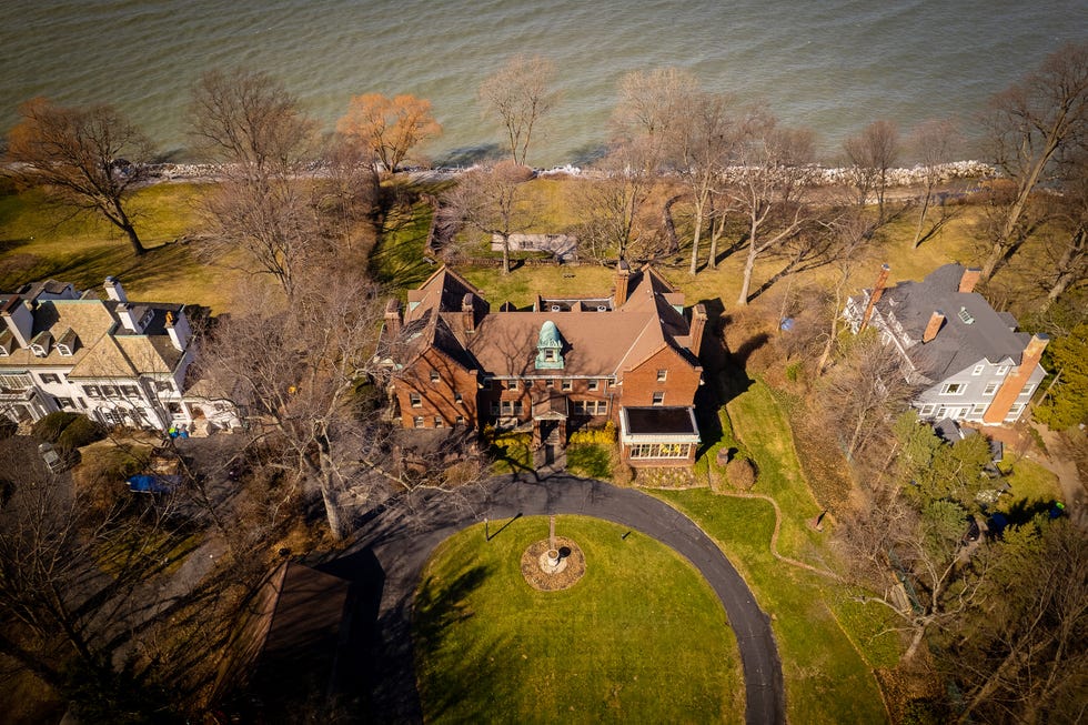 Aerial view of a large historic home surrounded by trees and grass near a shoreline.