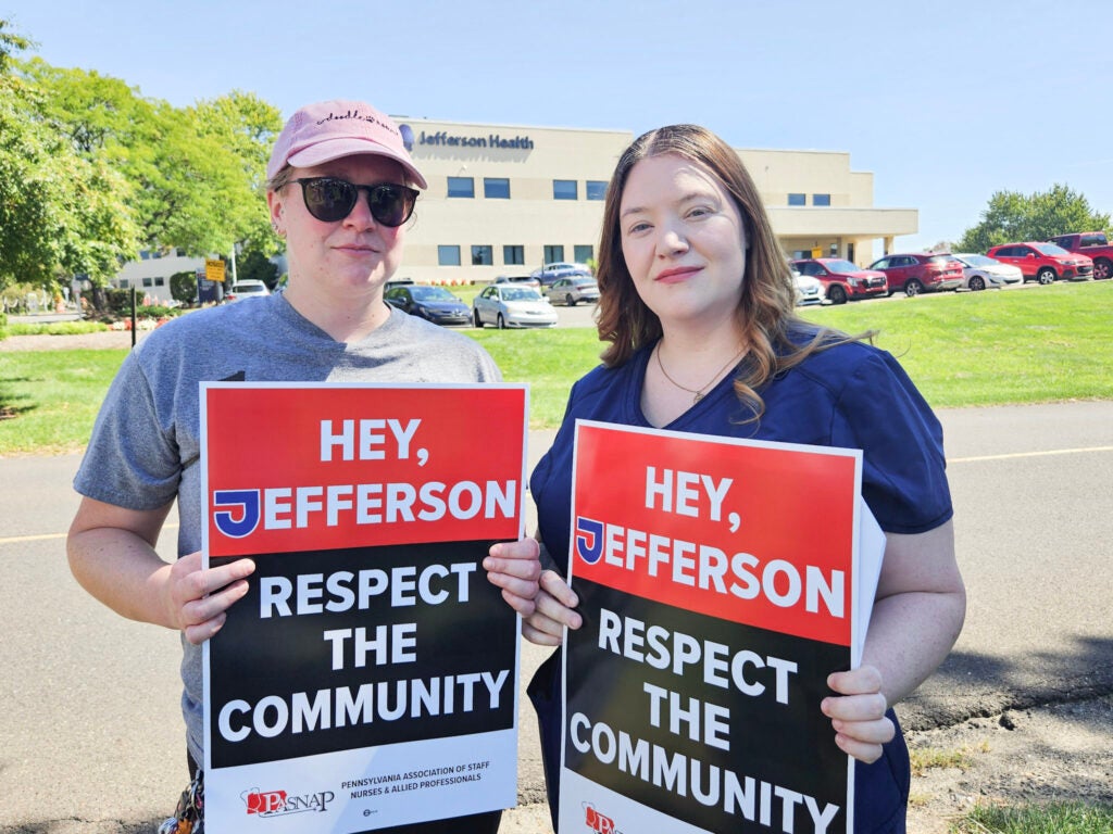 Two people hold signs reading HEY, JEFFERSON RESPECT THE COMMUNITY